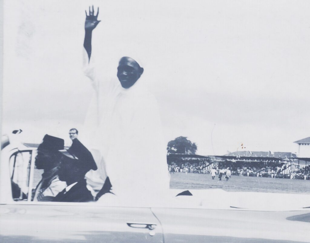 Sir Abubakar Tafawa Balewa standing in an open car on Independence Day, 1 October 1960